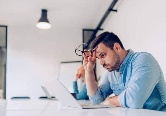 Exhausted young businessman using laptop at work and sitting by the desk while